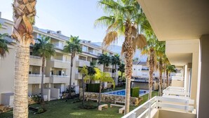 A hotel courtyard with palm trees, a swimming pool, and a white balcony railing.