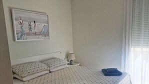 A bedroom with a bed, a ceiling fan, a painting on the wall, a window with curtains, and a bedside lamp.