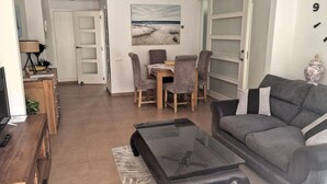 A living room with a sofa, coffee table, TV, and a dining area with chairs and a table.