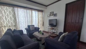 A living room with a sofa set, a coffee table, a TV on a stand, and a door.
