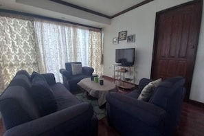 A living room with a sofa set, a coffee table, a TV on a stand, and a door.