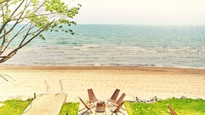 A beach with a concrete deck, four wooden lounge chairs, and a table. - Suite 209: Beautiful 2-Bedroom Beachfront Suite (Wainfleet)