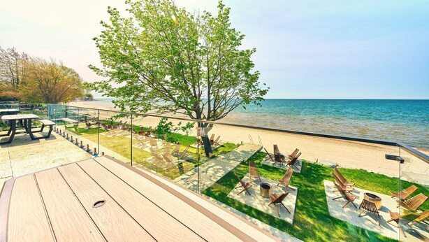 A deck with wooden flooring, outdoor seating, and a view of the sea. - Suite 209: Beautiful 2-Bedroom Beachfront Suite (Wainfleet)