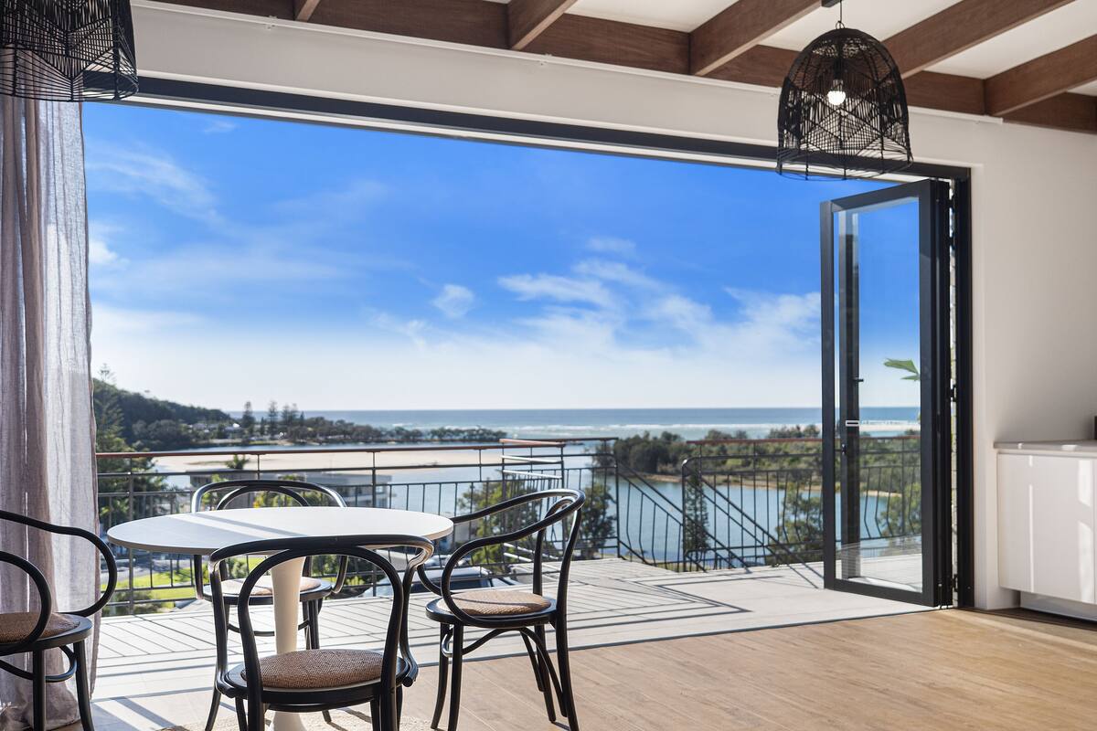 A balcony with a table and chairs, a view of the ocean, and a hanging light fixture.