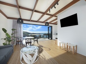 A modern living room with a glass table, a sofa, and a TV mounted on the wall. - The Beach Rooms (Nambucca Heads)