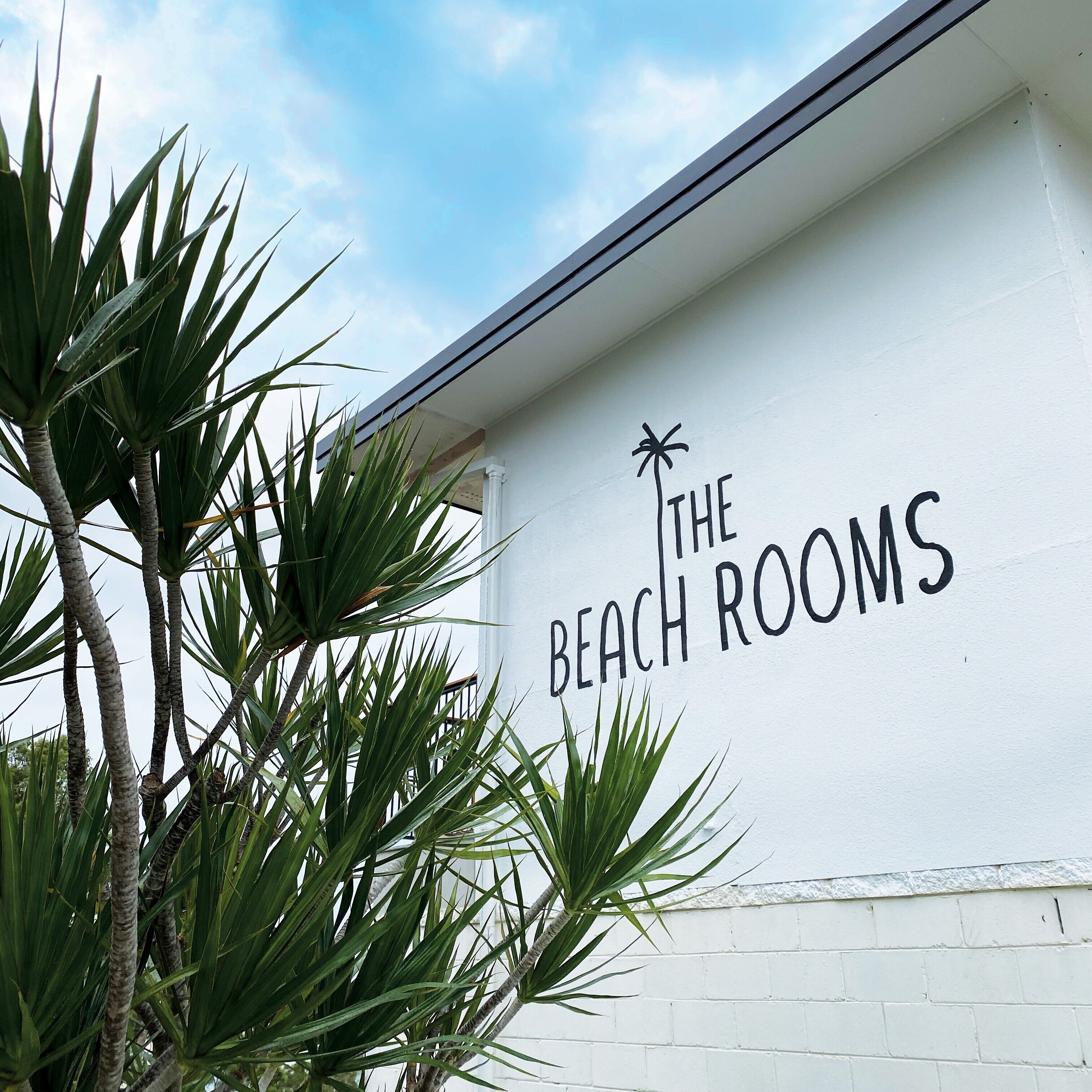A white building with a sign that reads "The Beach Rooms".