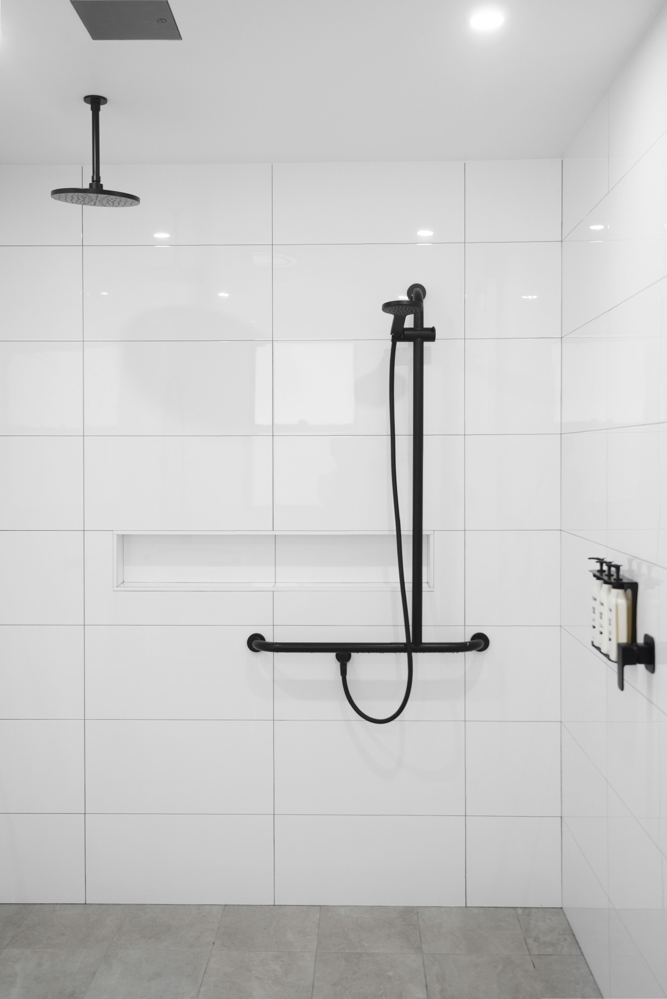 A modern bathroom with white tiled walls, a black showerhead, and a control panel.