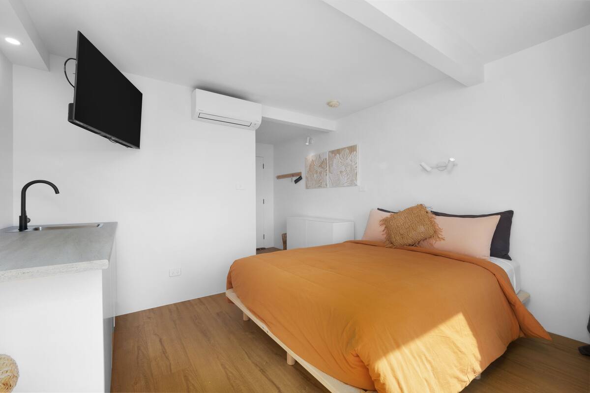 A bedroom with a bed, a TV mounted on the wall, a bedside table, and a wardrobe.