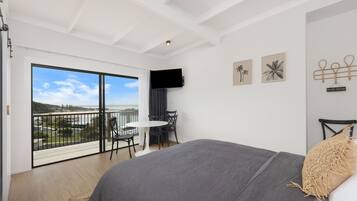 A bedroom with a large bed, a balcony with a view, a small table, and chairs.
