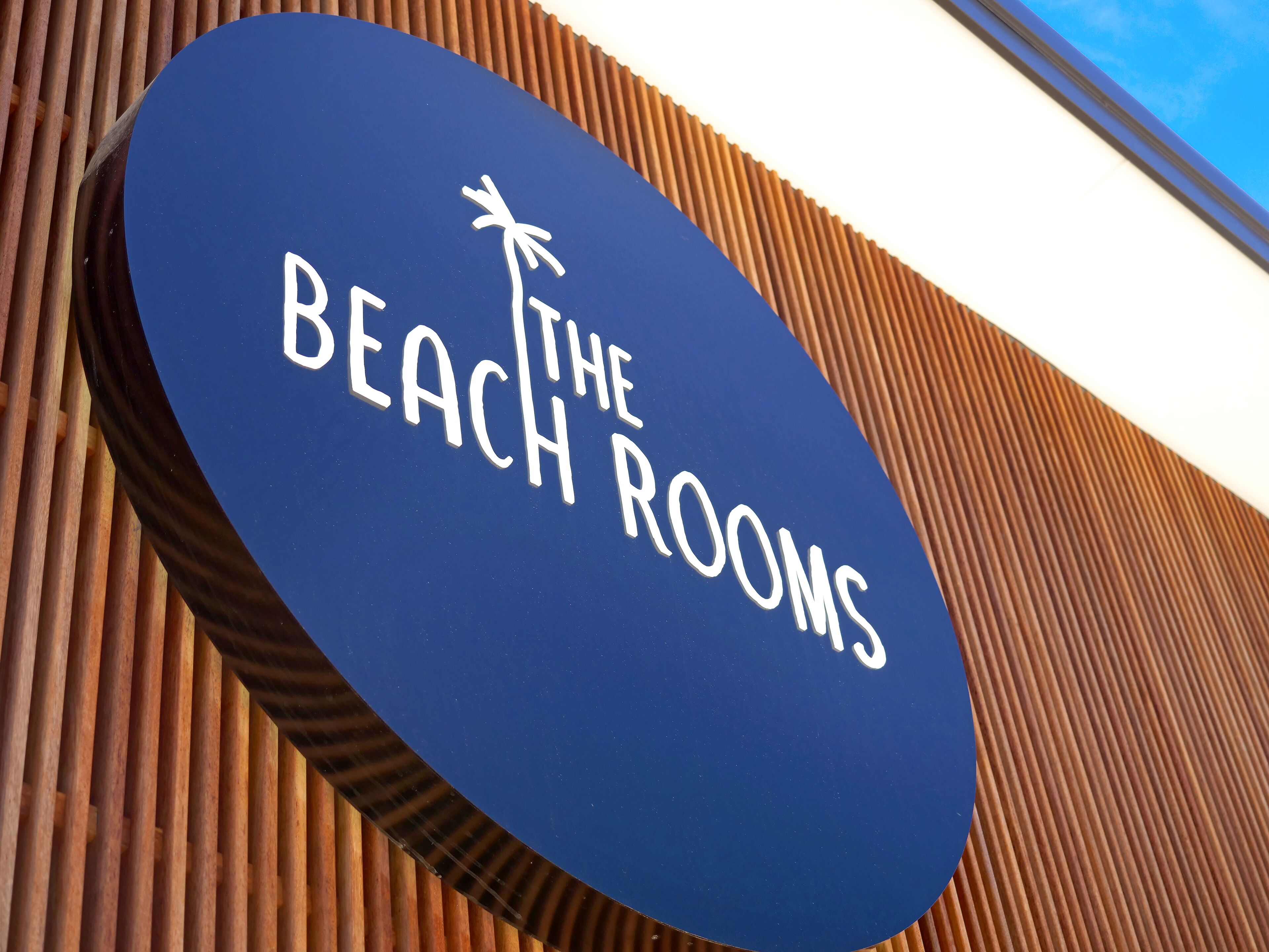 Een bordje met de tekst 'The Beach Rooms' en een palmboom symbool.