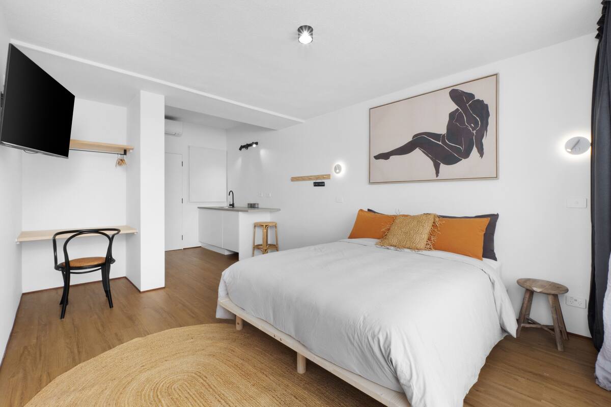 A modern bedroom with a bed, a desk, and a TV.