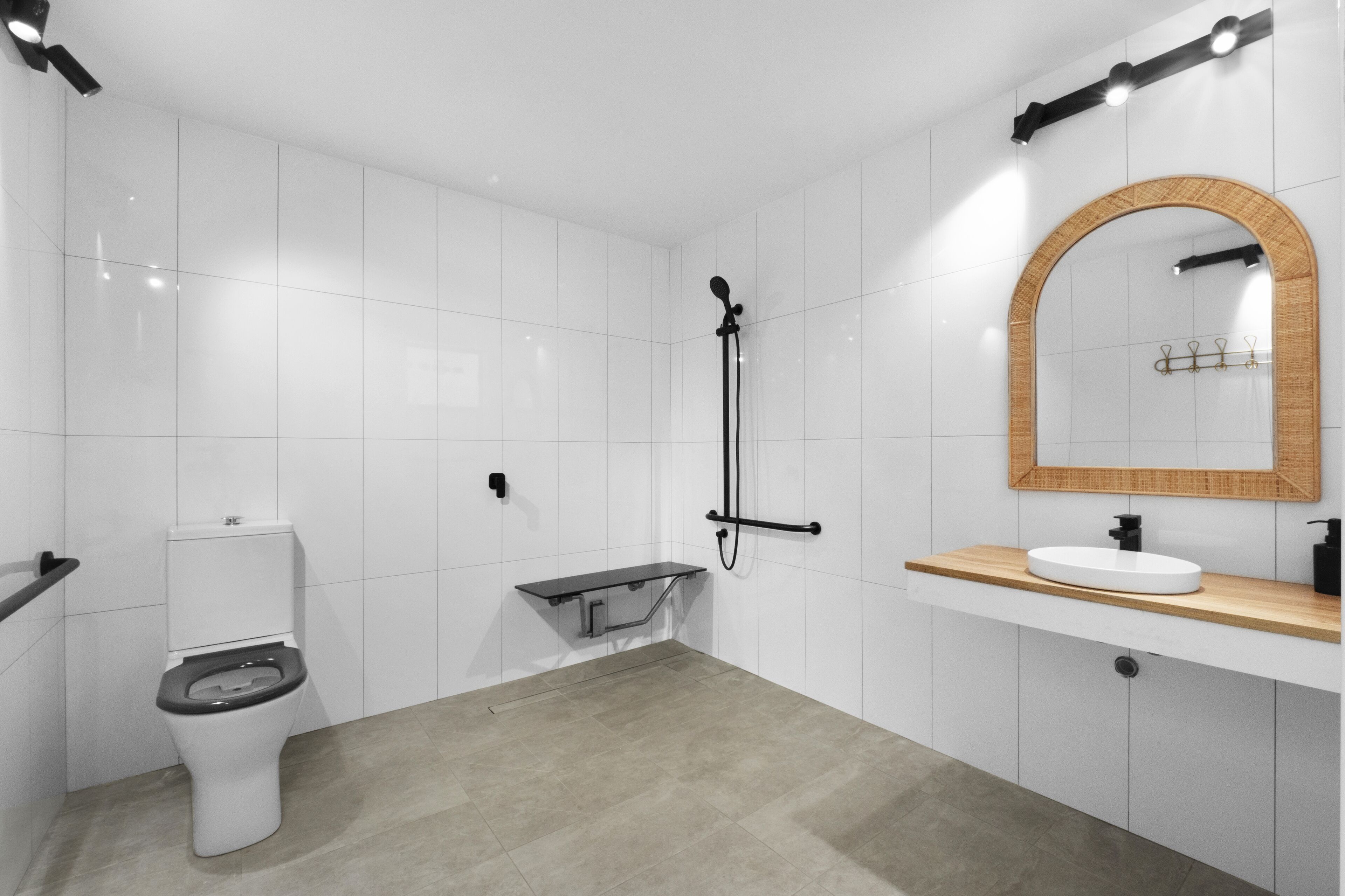 Een moderne badkamer met witte tegels, toilet, douche, wastafel met houten aanrechtblad en een spiegel met houten lijst.