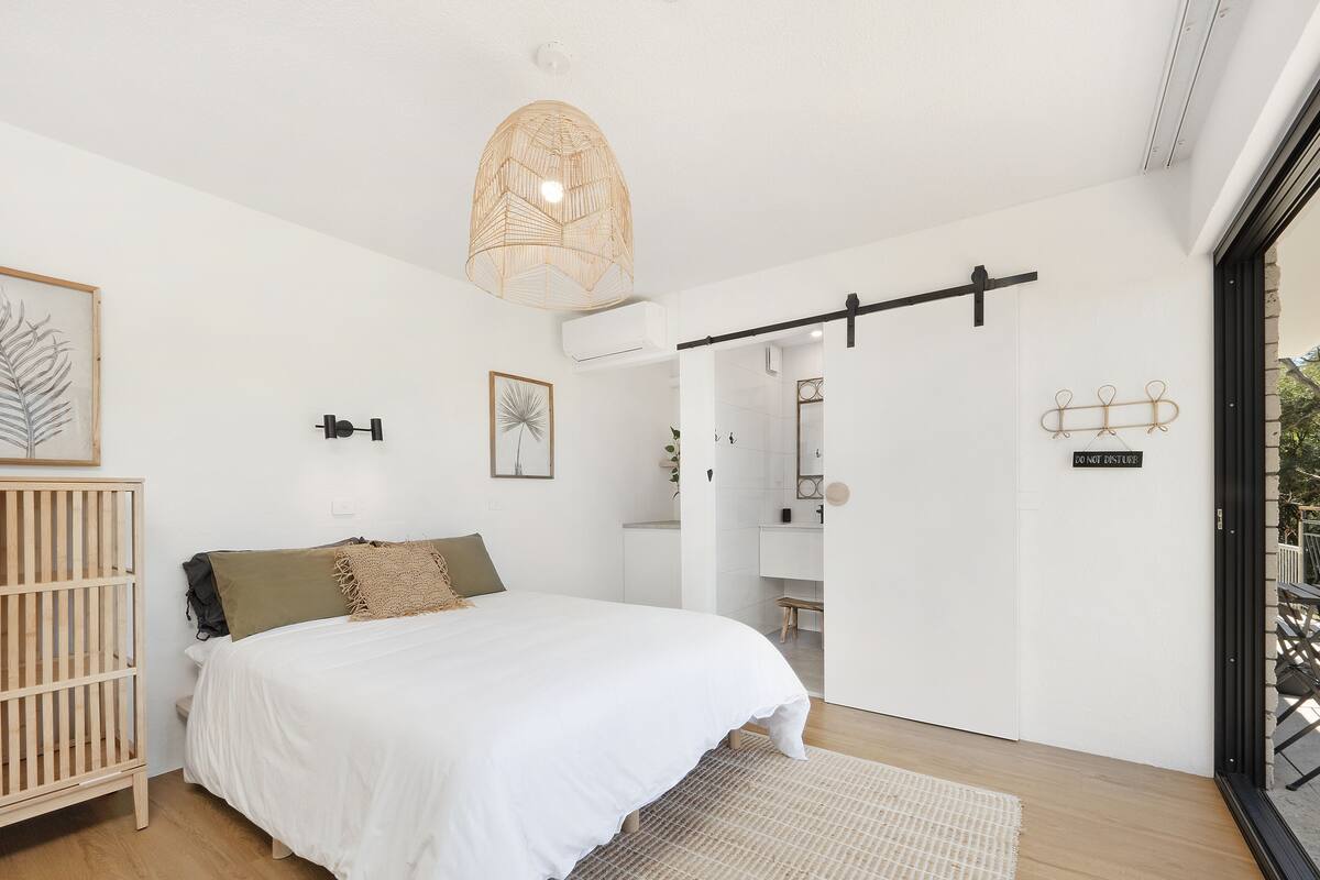 A bedroom with a bed, a crib, a large window, and a door leading to a balcony.