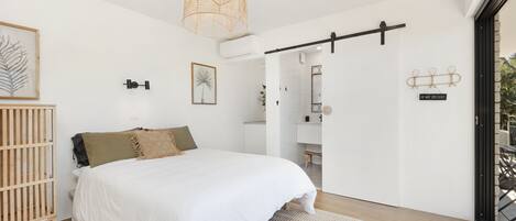 A bedroom with a bed, a crib, a large window, and a door leading to a balcony.
