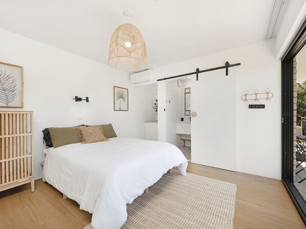 Ein Schlafzimmer mit einem Bett, einem Babybett, einem großen Fenster und einer Tür, die auf einen Balkon führt.
