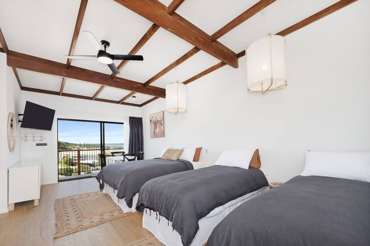 A bedroom with two beds, a ceiling fan, a TV mounted on the wall, and a balcony with a view.