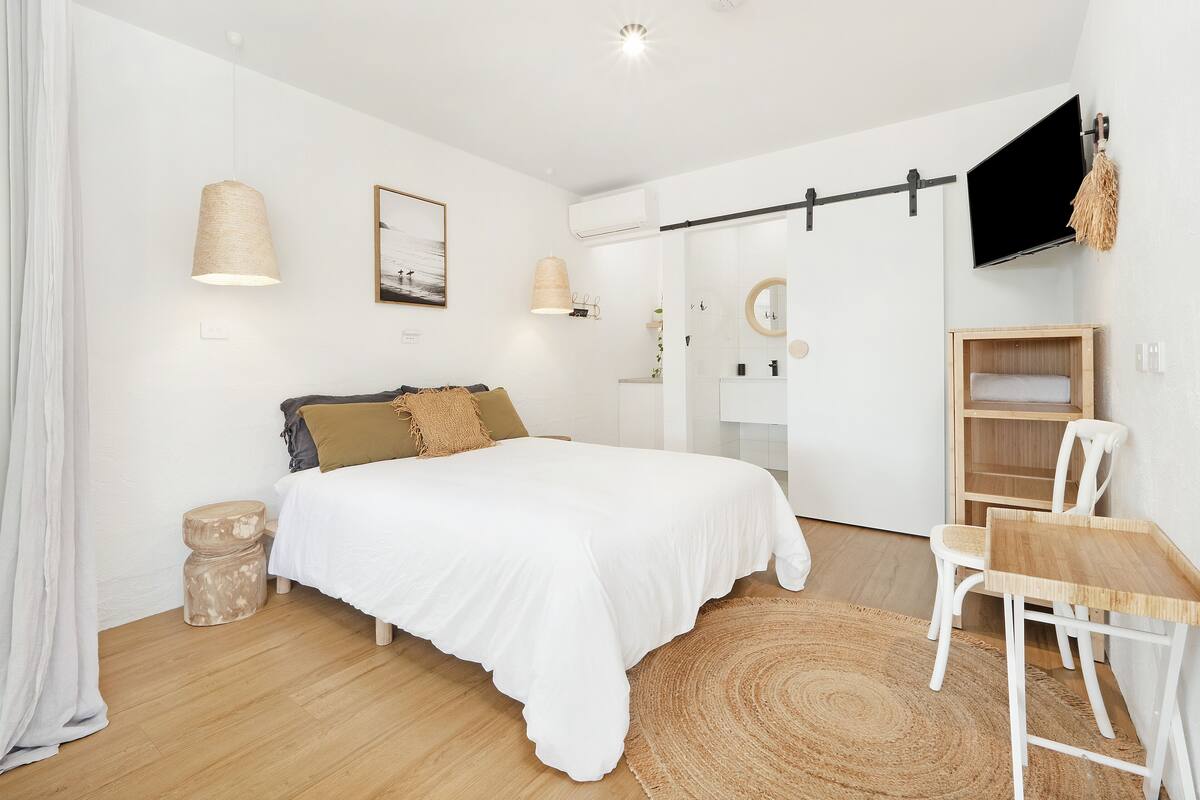 A modern bedroom with a bed, bedside table, and a TV mounted on the wall.