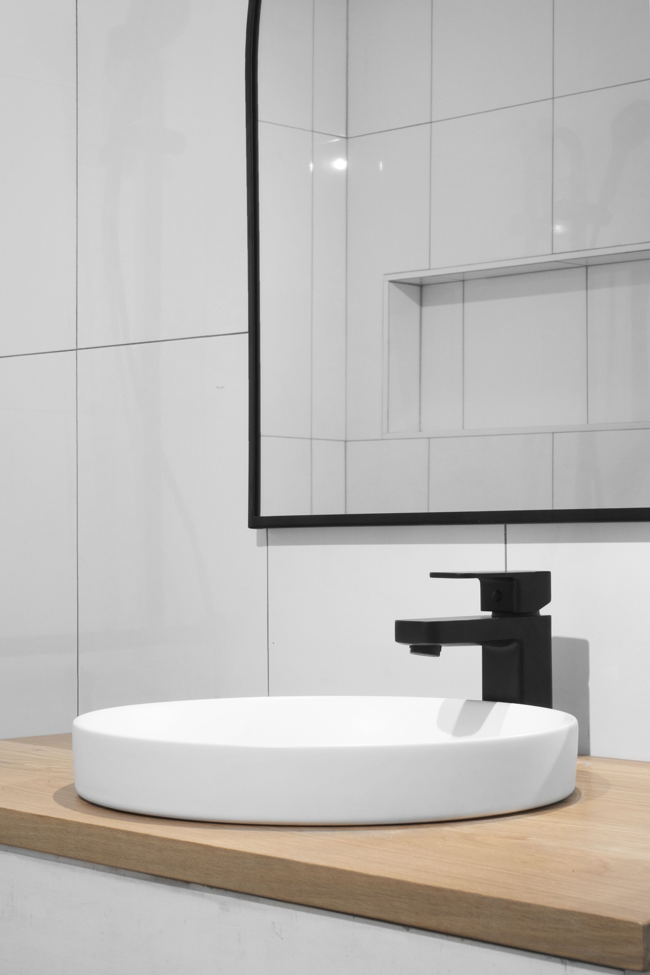 A modern bathroom with a white sink, black faucet, and a wooden countertop.