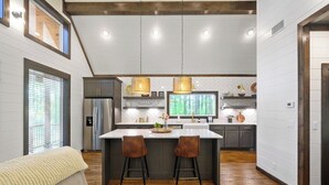 Een moderne keuken met een centraal eiland, barkrukken, hanglampen en een groot raam.