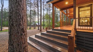 Een houten vakantiehuisje met een wenteltrap naar een overdekt terras, omgeven door bomen.
