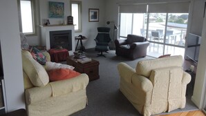 A spacious living room with a fireplace, comfortable seating, and large windows offering a view of the outdoors.