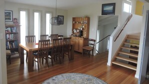 A spacious living room with a wooden dining table and chairs, a kitchen area with wooden cabinets, a staircase, and a view of the outdoors.