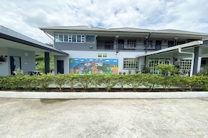 Un bâtiment à deux étages orné d’une fresque murale, doté d’un espace extérieur couvert avec des sièges et d’une entrée fermée par un portail.