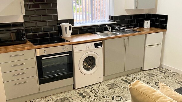 A compact kitchen with a microwave, oven, washing machine, and a sink. - 1 Bedroom St Helens Apartment | Free WiFi | Fully Furnished (St Helens)