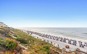 Une plage bordée de rangées de chaises longues et de parasols, une promenade en bois et un ciel dégagé.