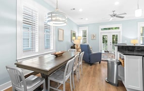 A modern kitchen with a dining area, featuring a wooden table, white chairs, a blue armchair, and a ceiling fan.