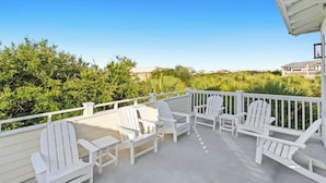 A covered outdoor deck with white Adirondack chairs and a railing, overlooking a lush landscape. - Spacious 30A Home Steps to Beach With King Suites and Loft Space (Panama City Beach)