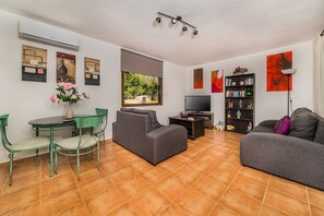 A living room with a sofa, a dining table with chairs, a TV, and a bookshelf. - Beautiful Villa "Enrique" with Mountain View, Pool, Wi-Fi, Garden & Terrace (POLLENÇA)