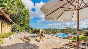 Un espace piscine doté d’un sol en pierre, de chaises longues et d’un parasol.