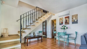 Un escalier avec des finitions en bois et des rampes noires, un coin repas avec une table ronde et des chaises, et un mur orné d’œuvres d’art abstraites.