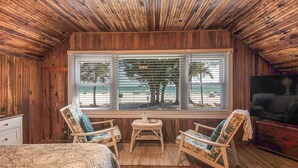 A wooden-paneled room with two lounge chairs, a small table, and a large window overlooking a beach. - Fun in the Sun  Gulf front, steps to the sand, 4-bed with spectacular views! (Anna Maria)