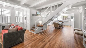 A spacious living area with a wooden floor, a wicker sofa, a dining table with chairs, and a staircase leading to another level. - Fun in the Sun  Gulf front, steps to the sand, 4-bed with spectacular views! (Anna Maria)