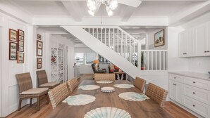 A spacious room with a wooden floor, white walls, a staircase, and a dining area with a table and chairs. - Fun in the Sun  Gulf front, steps to the sand, 4-bed with spectacular views! (Anna Maria)