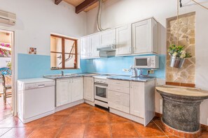 Une cuisine avec des meubles blancs, un lave-vaisselle, un four, un four à micro-ondes et un mur en pierre.