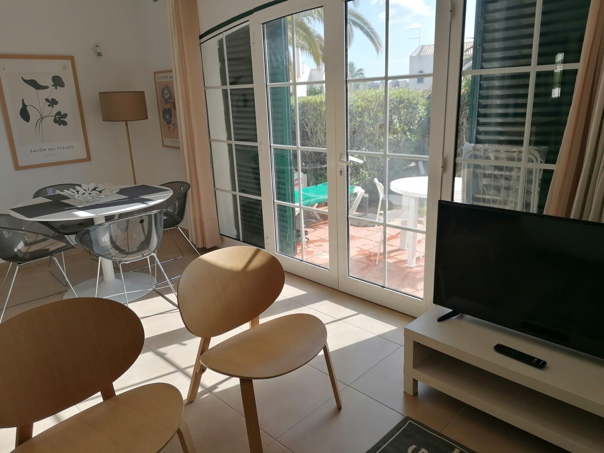 Un salon équipé d’un téléviseur, d’une table à manger avec des chaises, d’un canapé et d’une porte-fenêtre coulissante donnant sur une terrasse extérieure.