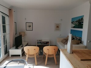 A modern living room with a TV, two wooden chairs, a sofa, and a coffee table. - Apartment 'Old Village Vilamoura' with Pool, Wi-Fi, A/C & Garden; Parking Available (Quarteira)