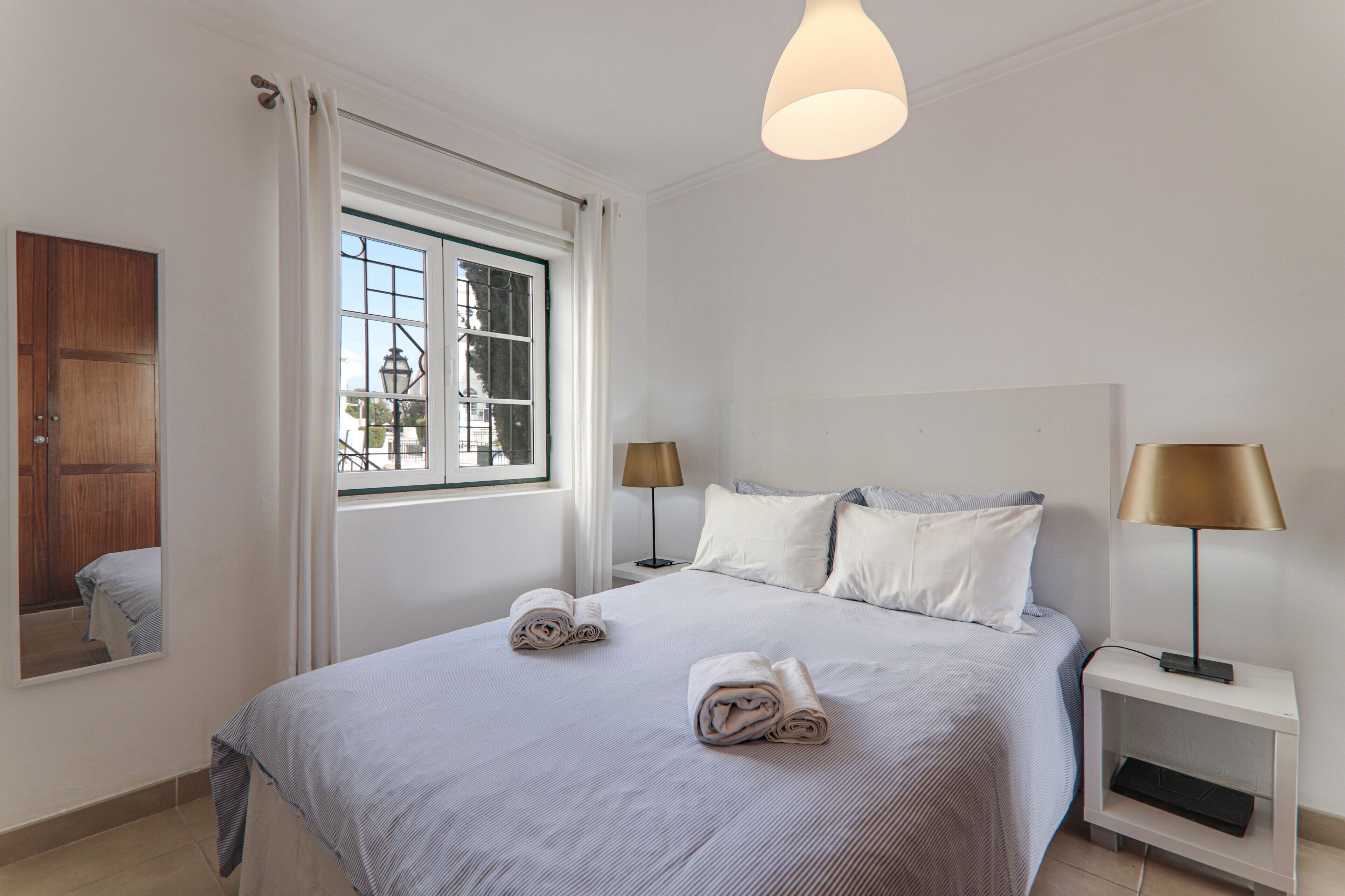 Une chambre d’hôtel avec un grand lit, deux tables de chevet, une fenêtre avec des rideaux et un luminaire suspendu.