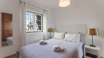 Une chambre d’hôtel avec un grand lit, deux tables de chevet, une fenêtre avec des rideaux et un luminaire suspendu.