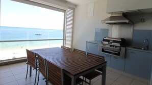 Un balcón con vistas al mar, una mesa de madera con sillas y una parrilla incorporada.