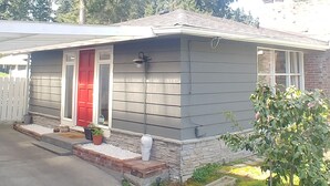 A single-story house with a grey siding exterior, a red front door, and a small porch area with potted plants. - Cool Mid-Century Bungalow!  (Vancouver)