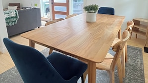 A modern dining area with a wooden table and blue chairs, a grey sofa, and a decorative wall piece. - Cool Mid-Century Bungalow!  (Vancouver)