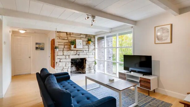 A modern living room with a stone fireplace, a large TV, and a blue sofa. - Cool Mid-Century Bungalow!  (Vancouver)