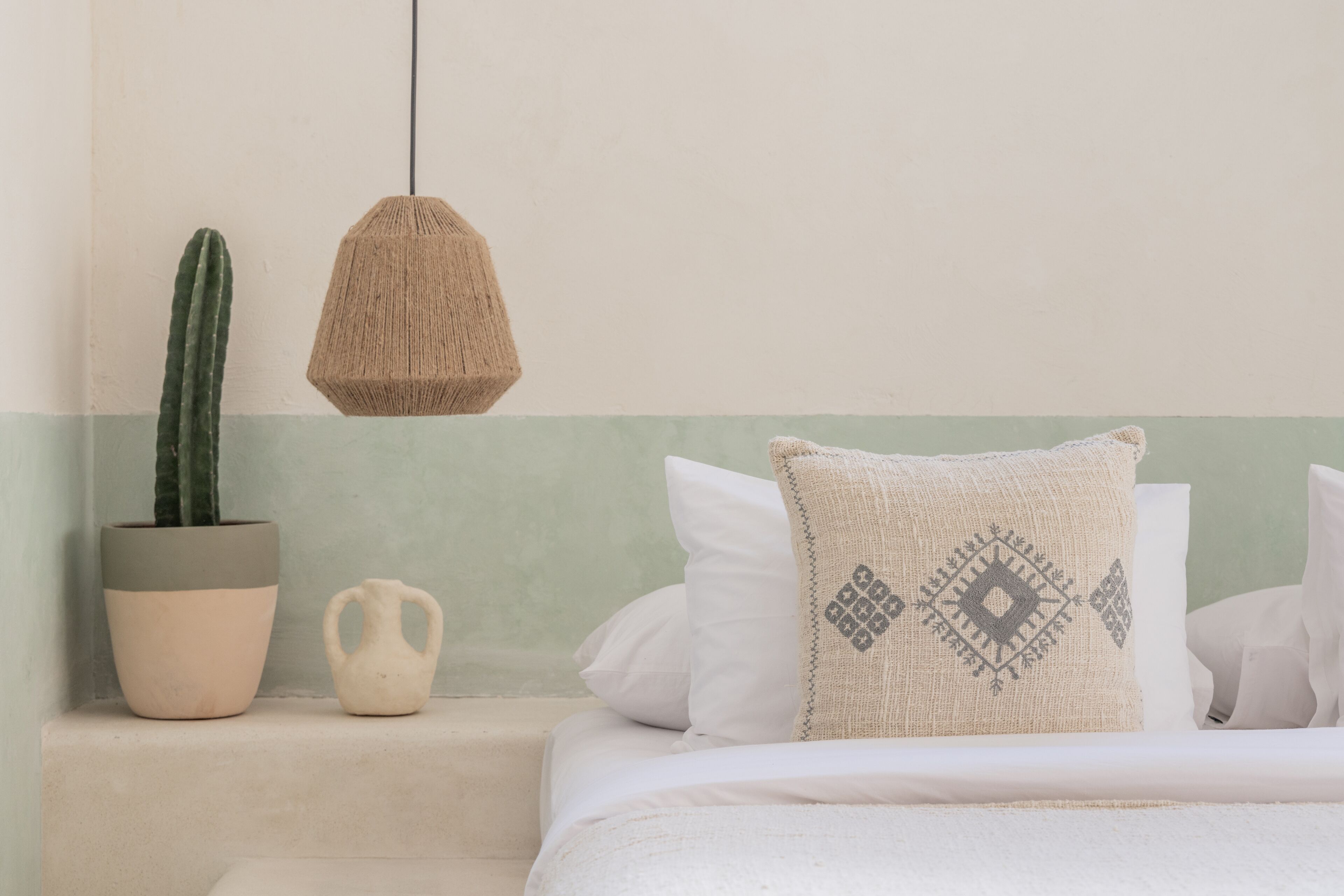 A bedroom with a bed, a hanging light, a potted cactus, and a decorative pillow.
