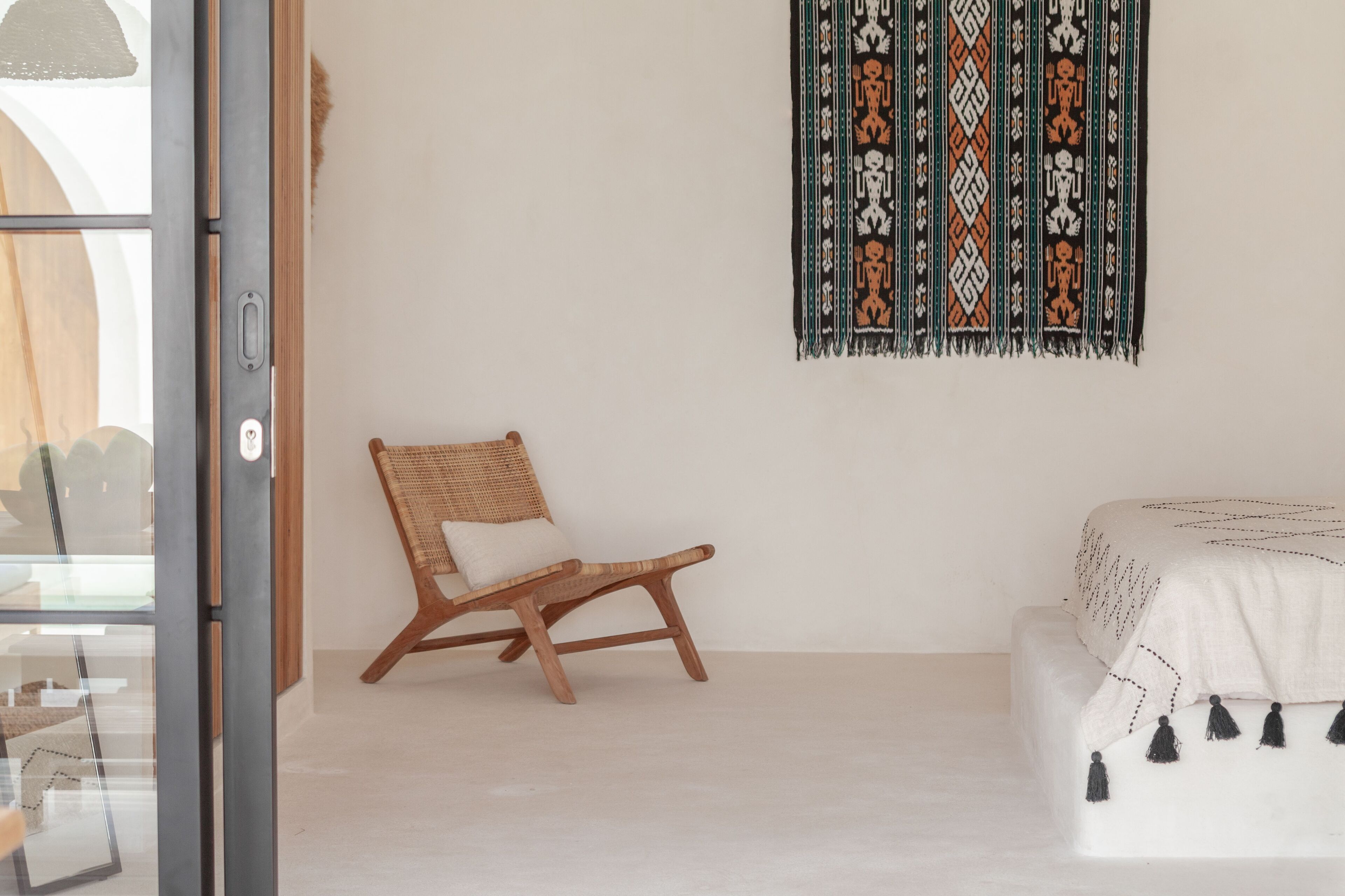 Una habitación con una mecedora de madera, una cama blanca con una colcha estampada y un adorno en la pared.