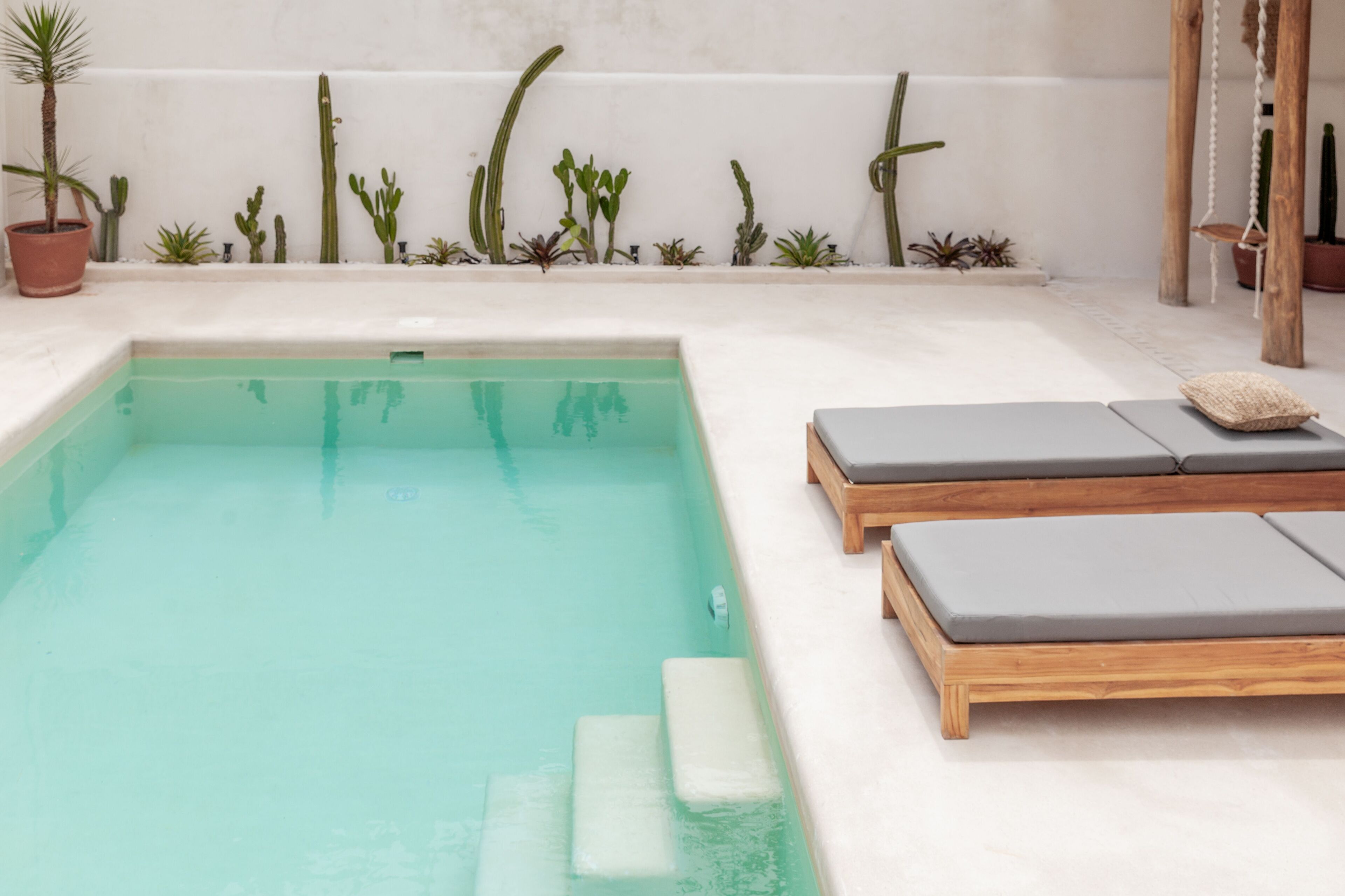 Ein rechteckiger Pool mit Stufen, umgeben von Holzliegen mit Kissen.