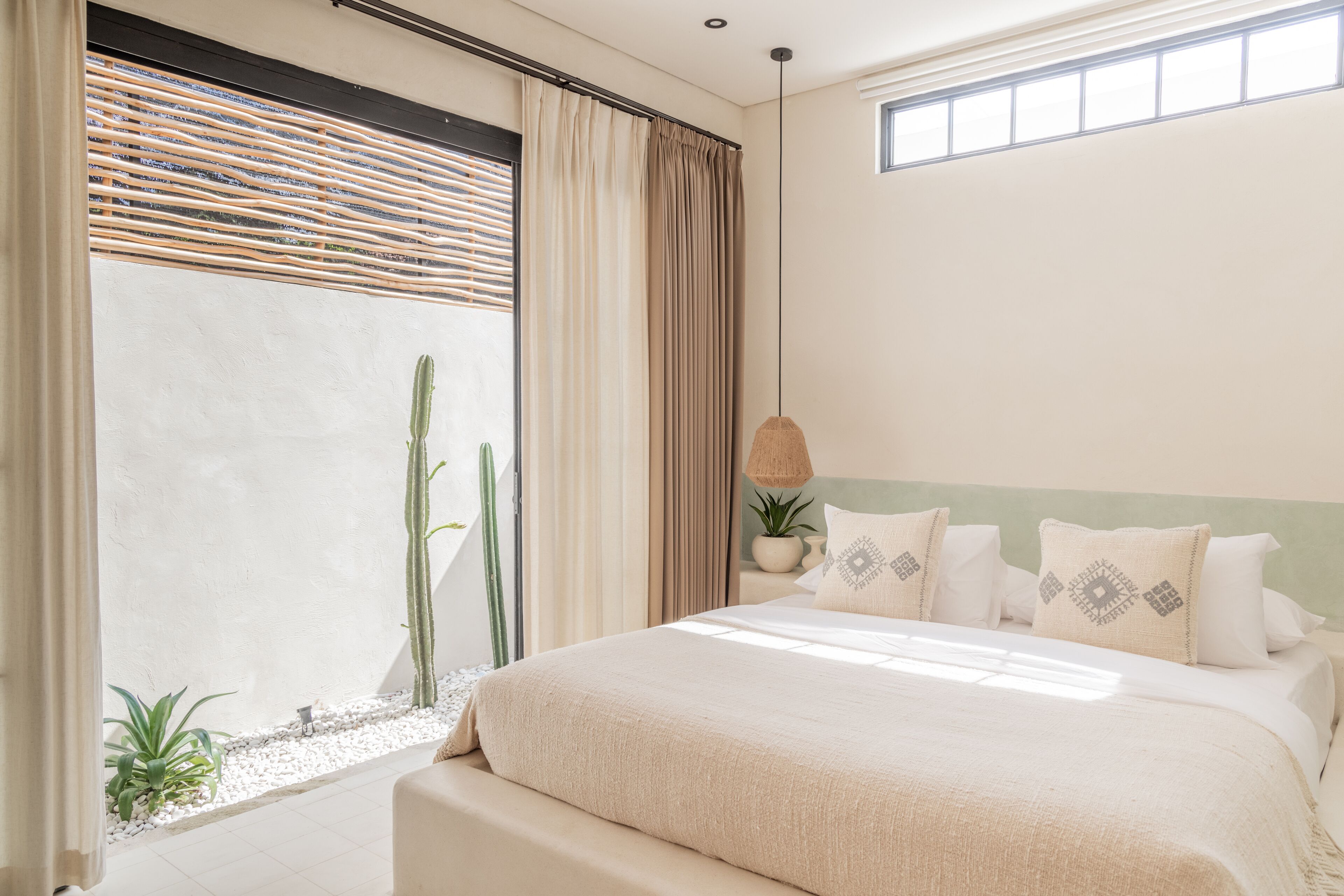A bedroom with a large bed, a potted plant, and a window with curtains.